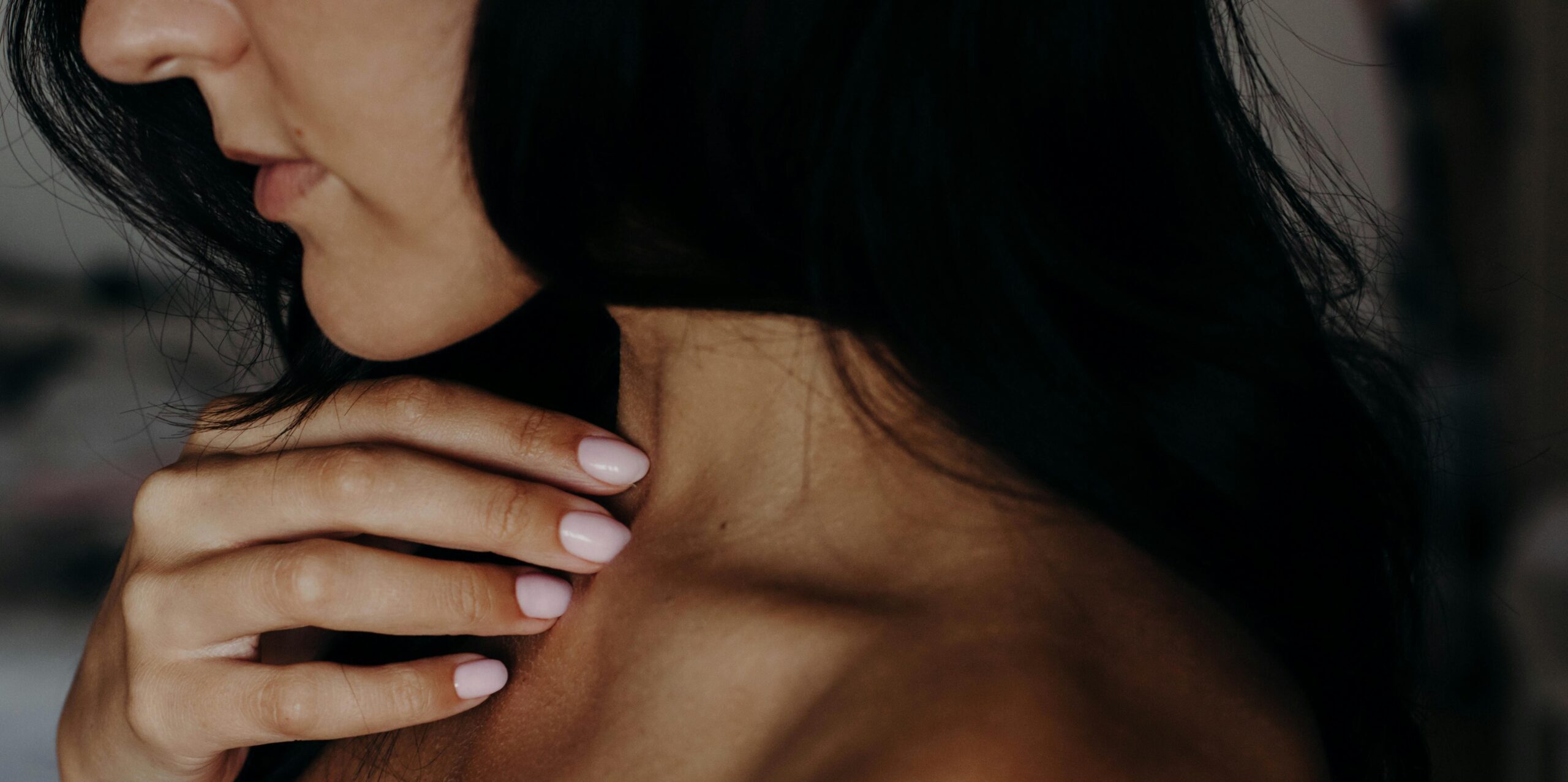 Intimate close-up of a young woman's neck, shoulder, and hand with a gentle touch, showcasing natural beauty.